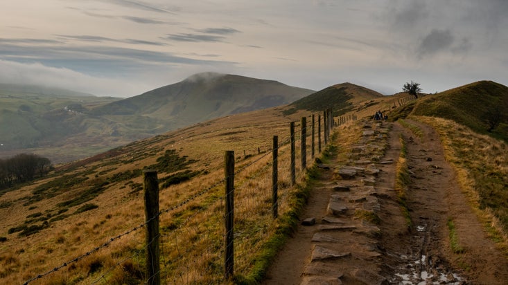 A footpath alongside a wire fence through a moody landscape with hills in the distance